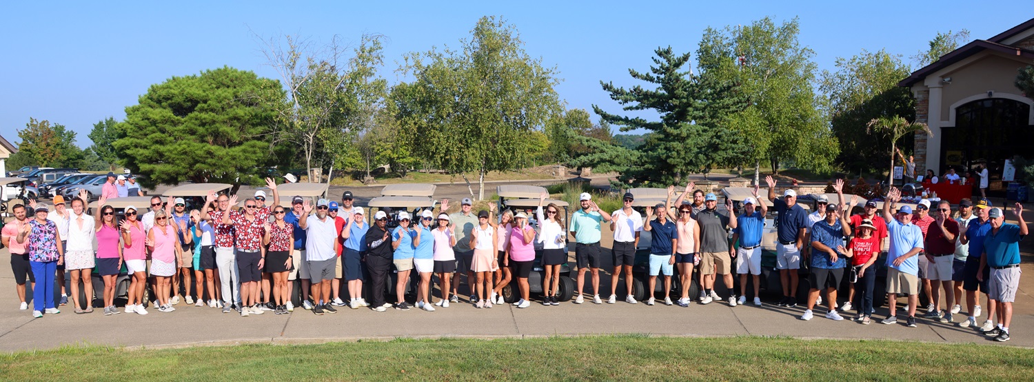 Overhead photo of a large group of golfers standing in front of two lines of golf carts.